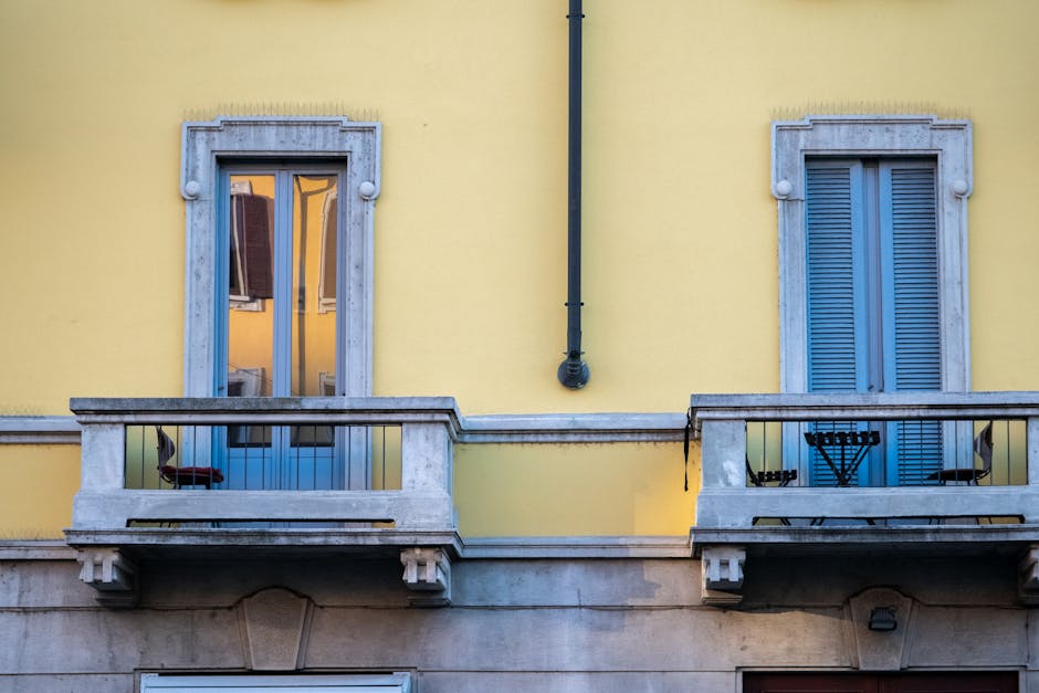 Yellow urban building facade with balconies and windows in daylight.