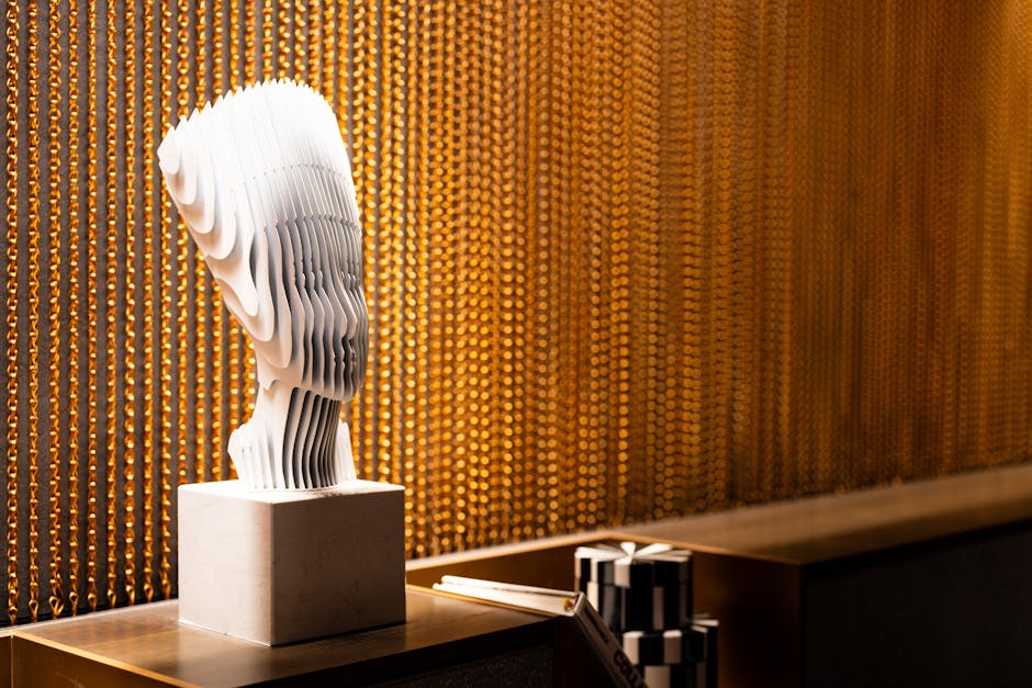 A striking modern abstract sculpture showcased against a backdrop of golden chains under spotlight.